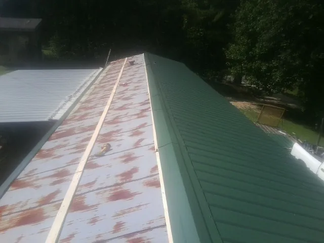 Old rusted panels beside newly installed green metal roofing — Wind Damage Roof Repair by Roofing Brothers in Lorane