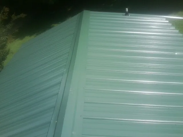 New green metal panels meeting at the ridge of a roof — Flat Roof Repair work by our crew in Lorane