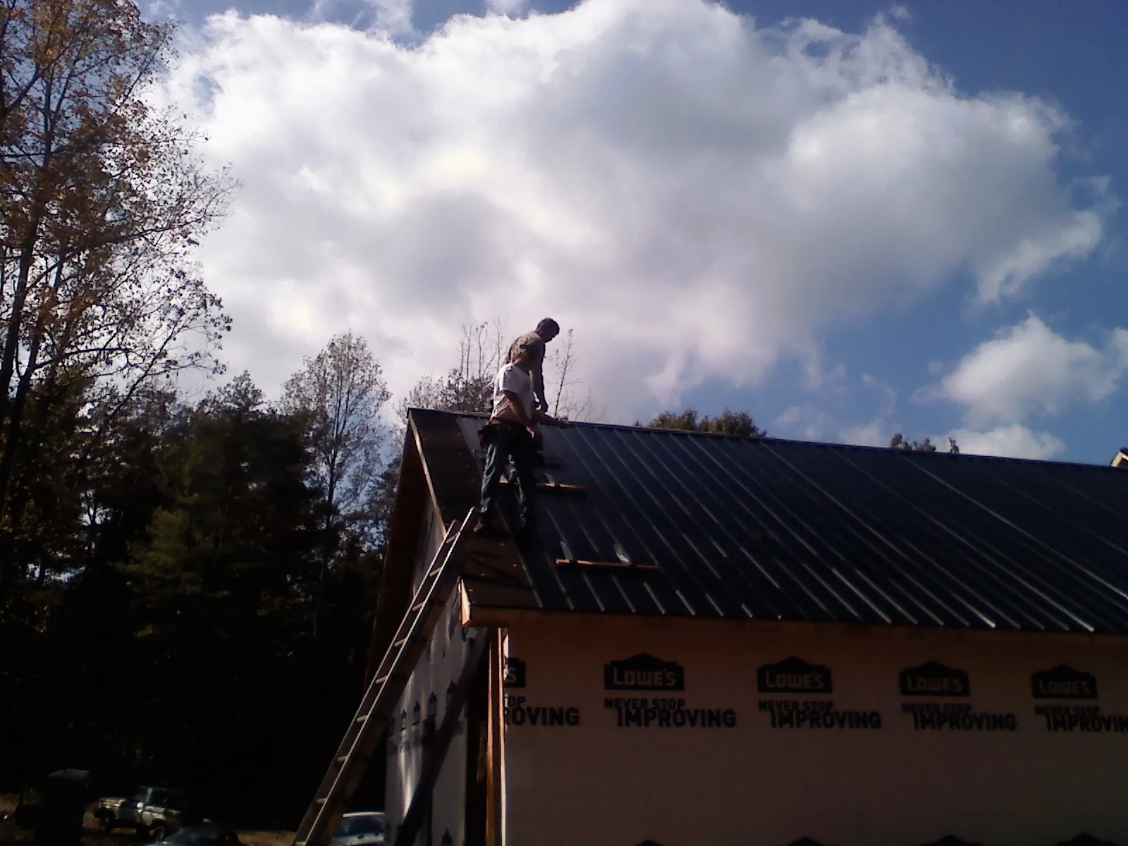 Roofer fastening dark metal panels high against a cloudy sky, from a Roof Inspection job in Lorane