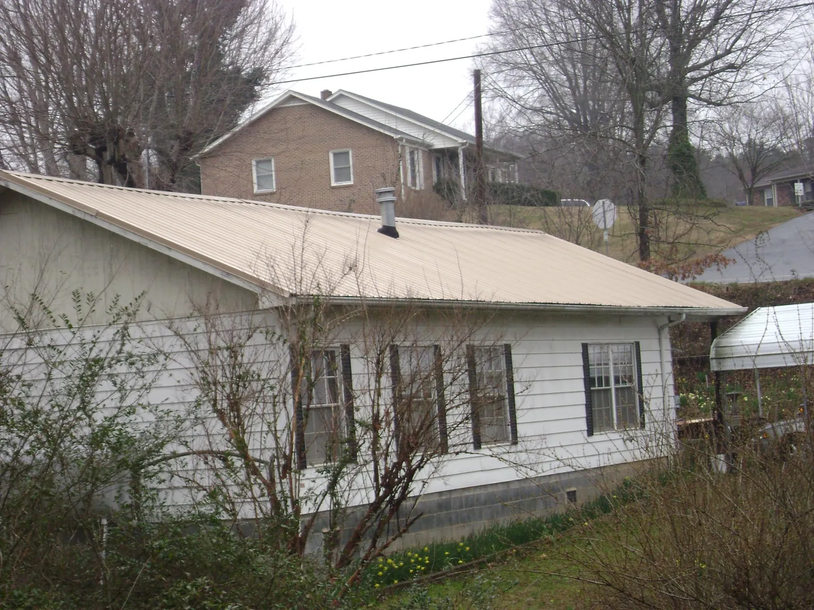 Tan metal roof on a white sided house set into a hillside — Commercial Roofing by Roofing Brothers in Lorane